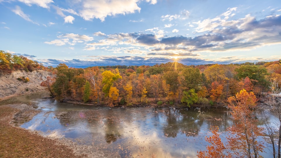 A river reflecting trees with autumn foliage, surrounded by hills.