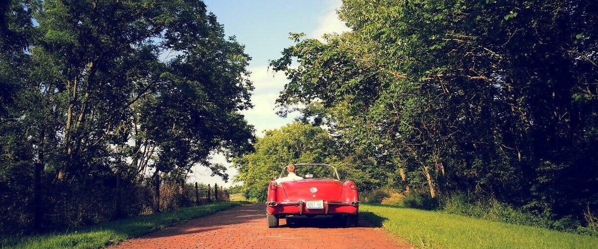 A red convertible car parked on a brick road surrounded by lush greenery.