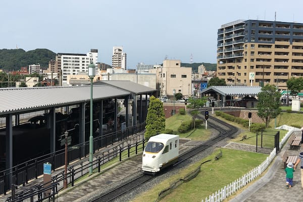 A train station with a white train on tracks, surrounded by buildings and greenery.