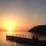 Un atardecer sobre un lago tranquilo con un muelle y dos personas sentadas allí.