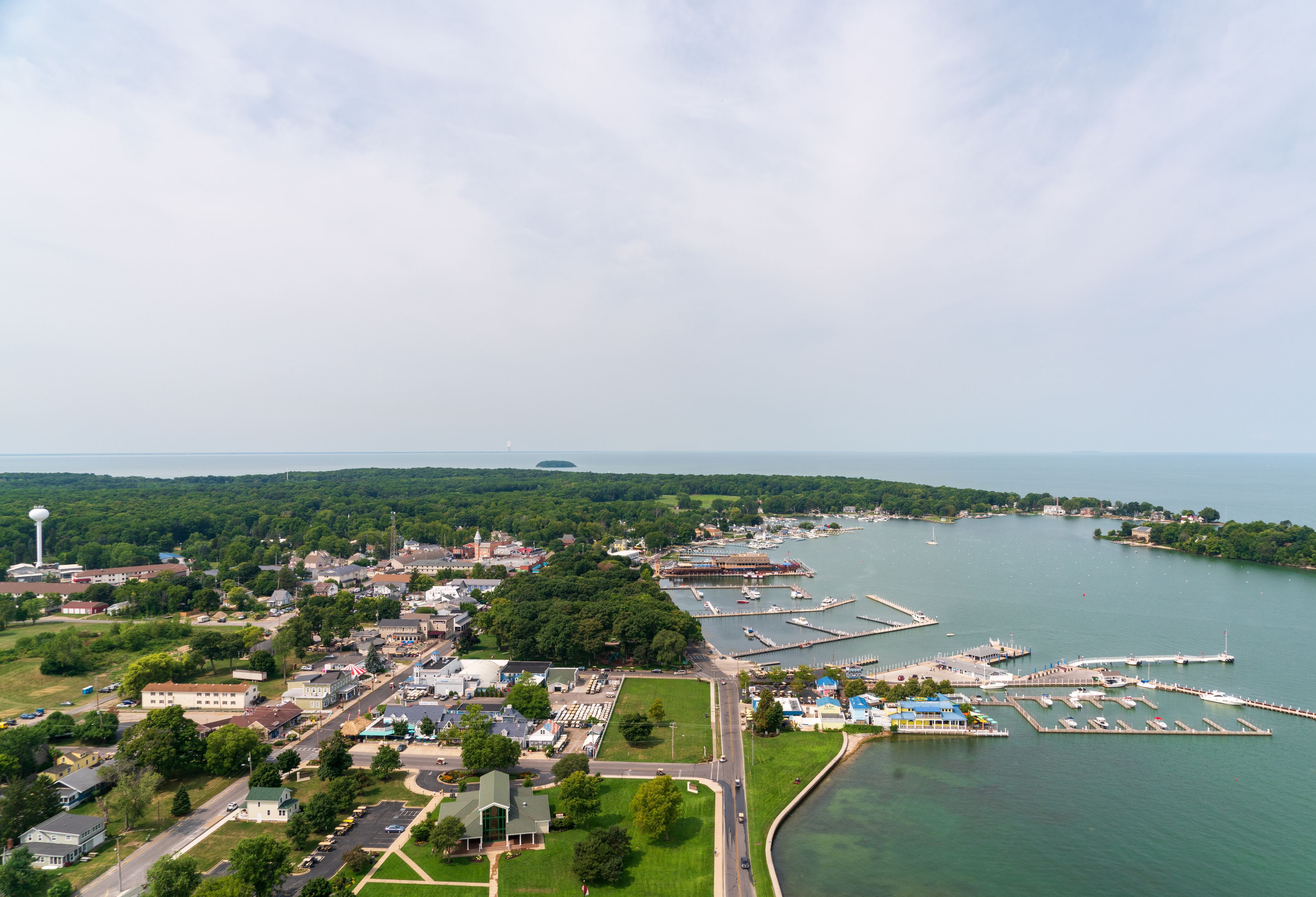 A coastal town with a marina, green hills, and a lighthouse.