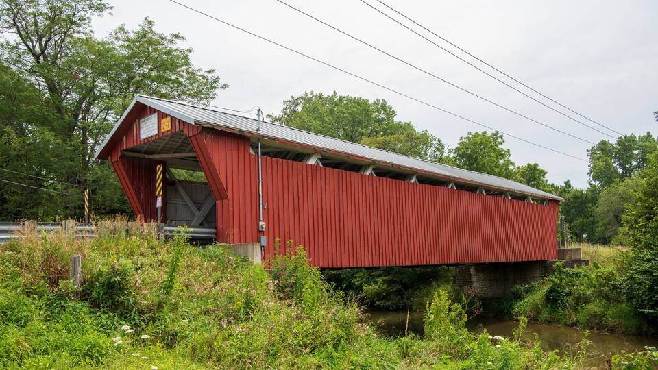 A red covered bridge over a river with lush greenery around.