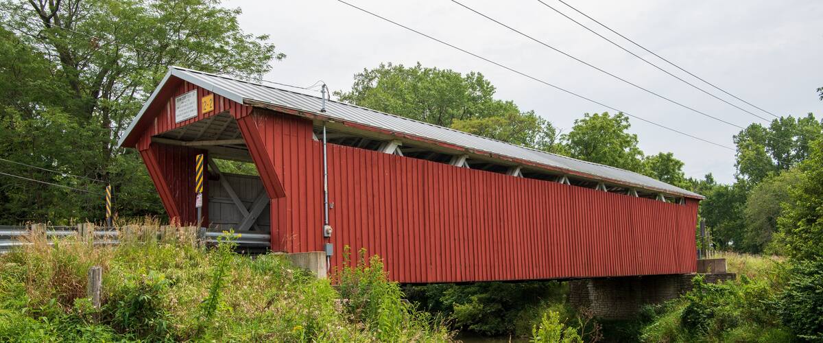 A red covered bridge over a river with lush greenery around.