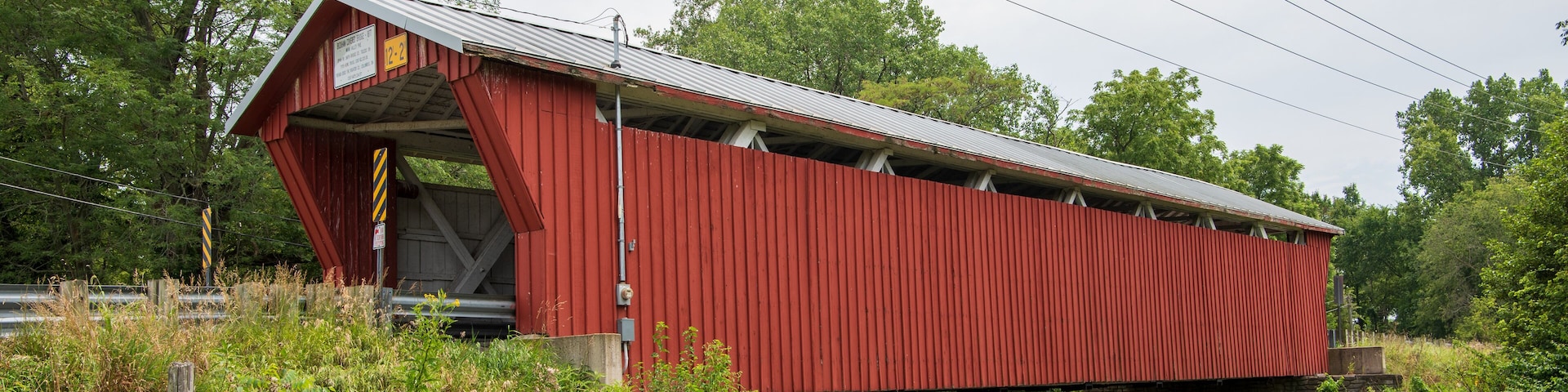 A red covered bridge over a river with lush greenery around.