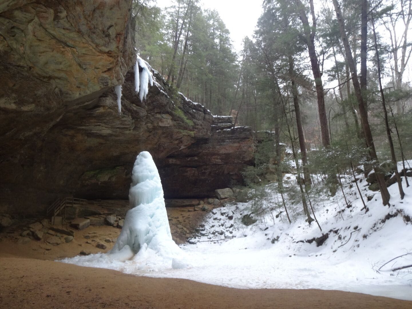 A snow-covered landscape with a large rock formation and a tall ice structure in the foreground.
