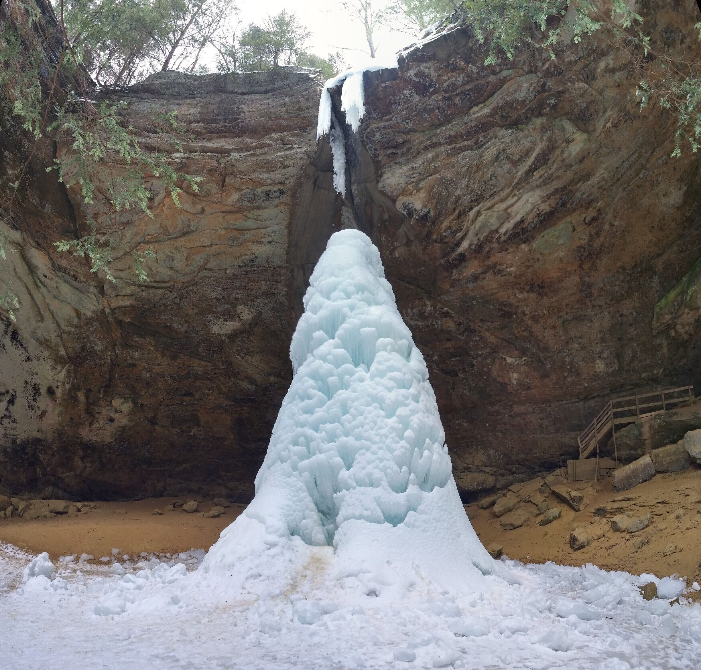A waterfall cascading into a snow-covered pool surrounded by rocky cliffs and sparse vegetation.
