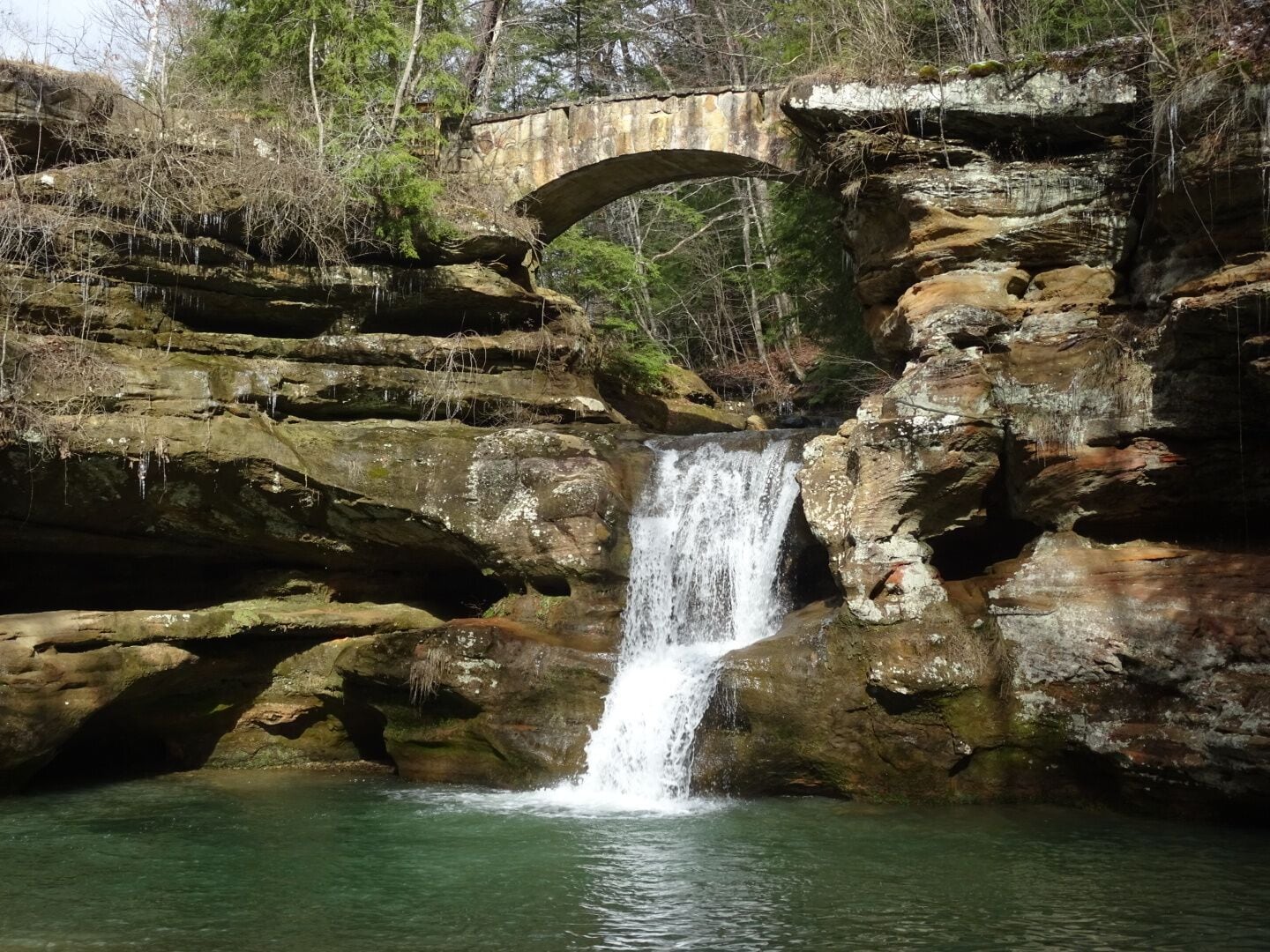 A waterfall cascading over rocky terrain beneath a stone bridge.