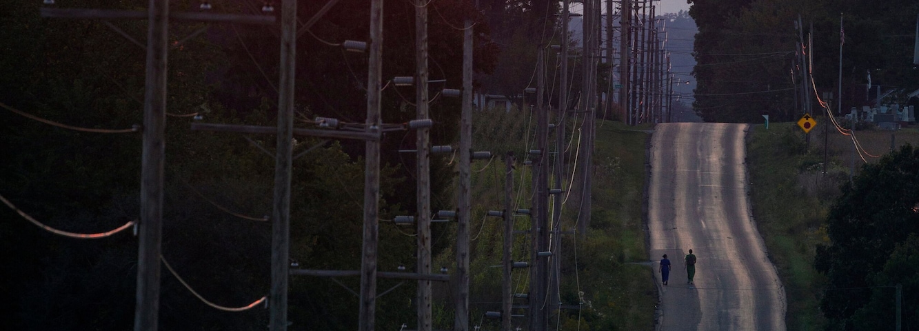 Una carretera con un atardecer al fondo, rodeada de árboles y postes de electricidad.