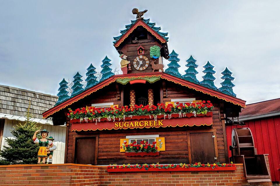 Un edificio de madera con un reloj, adornado con flores rojas y un letrero que dice "Sugar Creek".