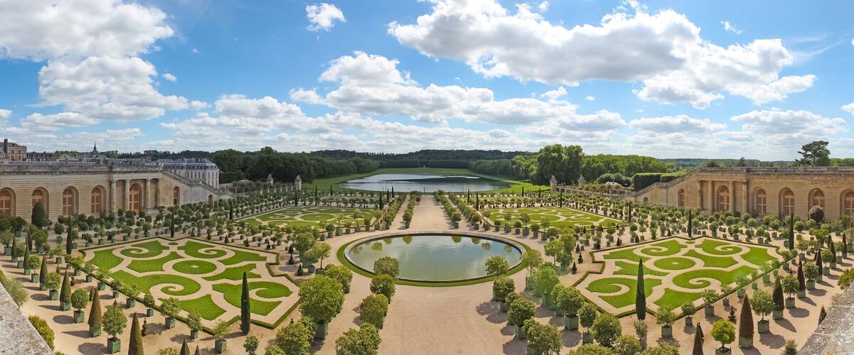 A formal garden with symmetrical pathways, a central pond, and classical architecture.