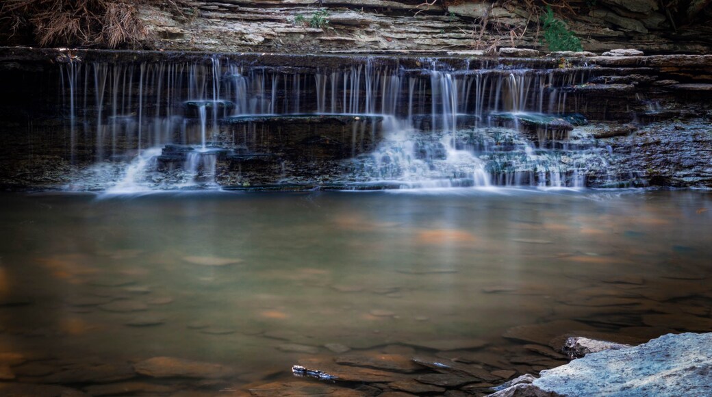 Uma cascata em vários níveis deságua sobre um afloramento rochoso em uma piscina calma.
