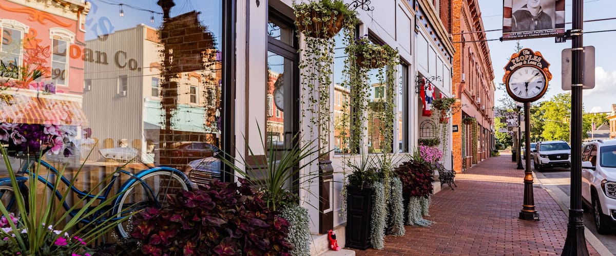A brick-paved street with hanging plants, a bicycle, and a vintage clock.