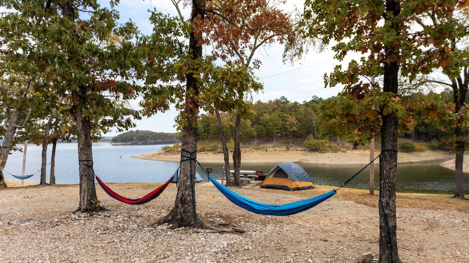 A hammock between trees, a tent, and a lake.