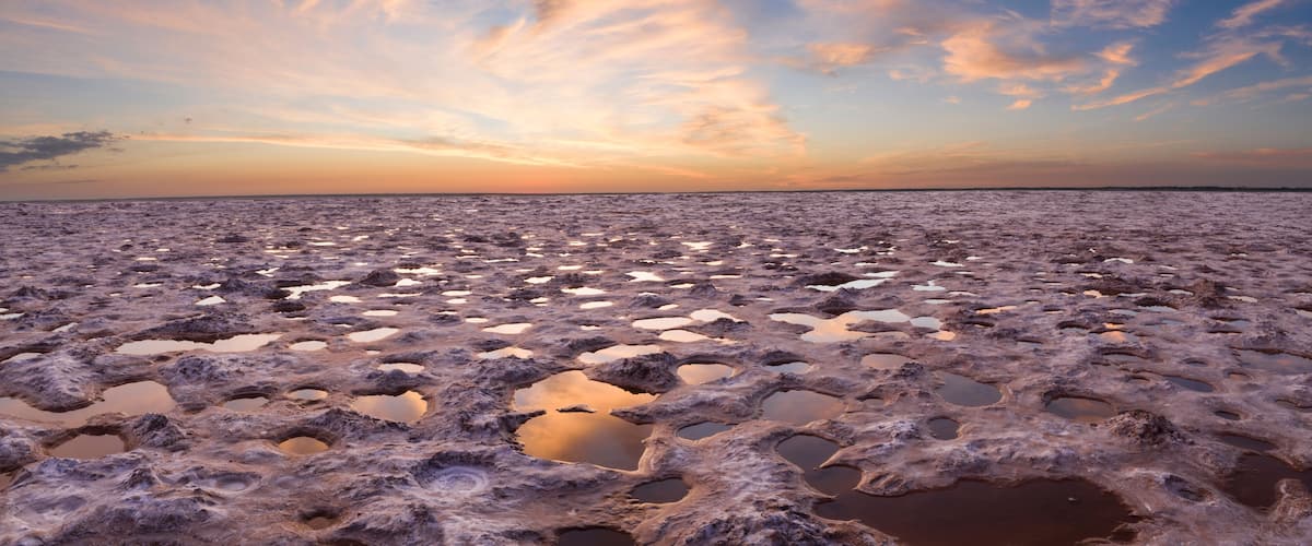 A salt flat with numerous circular pools of water under a sunset sky.