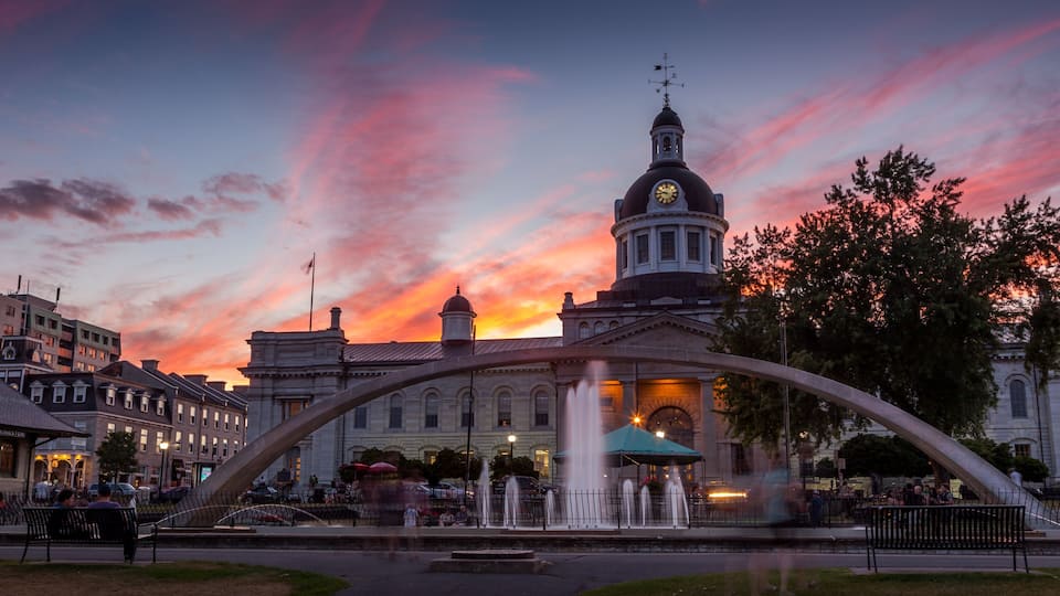 A sunset with a pink sky, a clock tower, and a fountain in a public square.