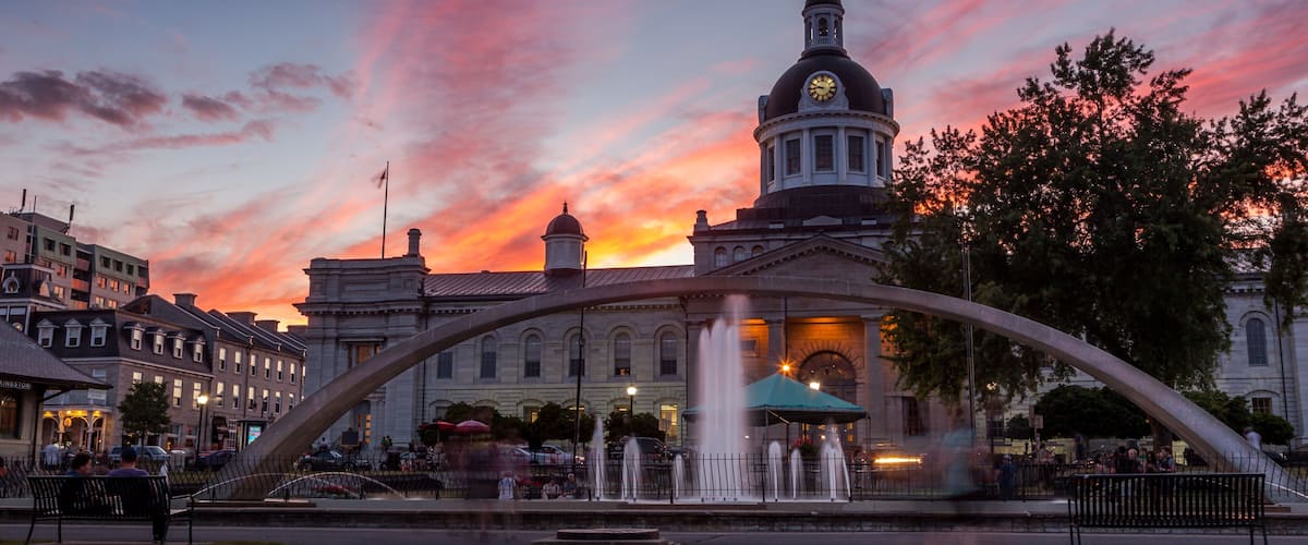 A sunset with a pink sky, a clock tower, and a fountain in a public square.