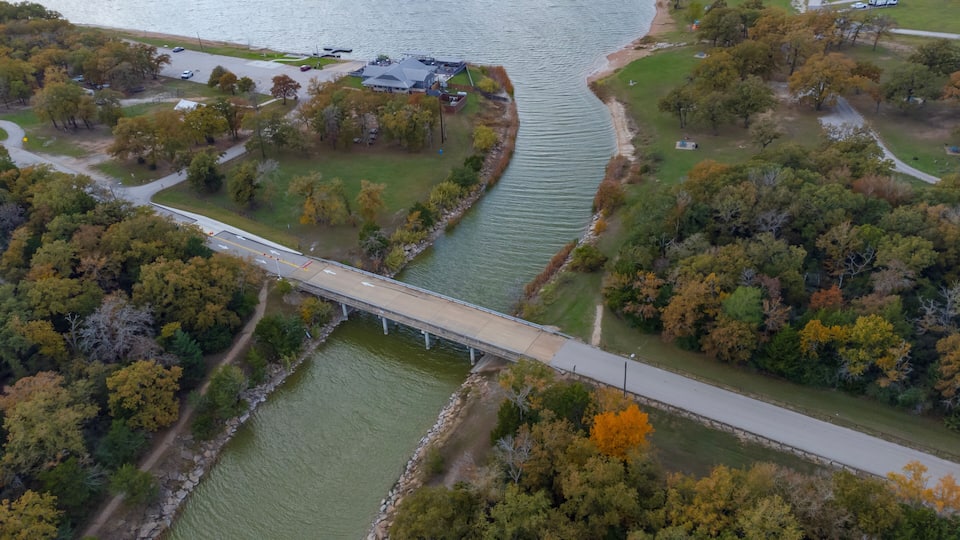 A bridge over a river, surrounded by trees and a parking area.