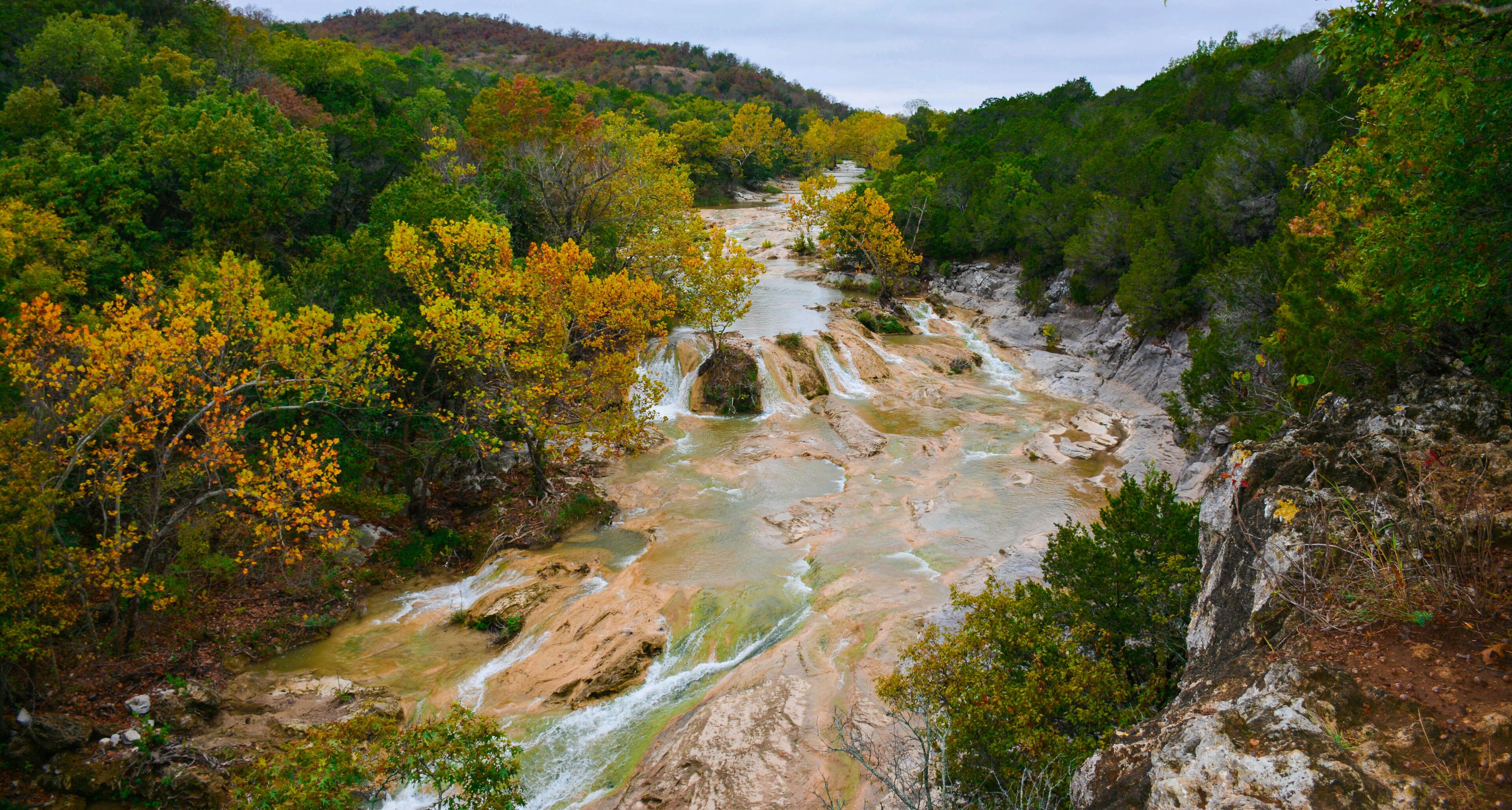 A river flowing through a forested valley with rocky terrain and autumn-colored trees.