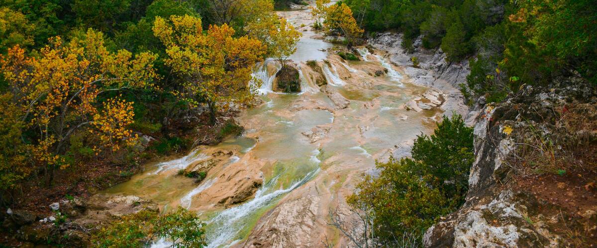 A river flowing through a forested valley with rocky terrain and autumn-colored trees.
