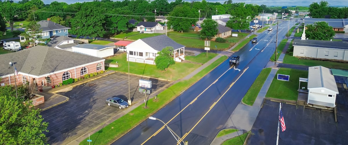 West Gentry Avenue in downtown Checotah, small town in McIntosh County, Oklahoma, mix of commercial buildings, churches, schools, residential neighborhood large houses, lush green trees, aerial