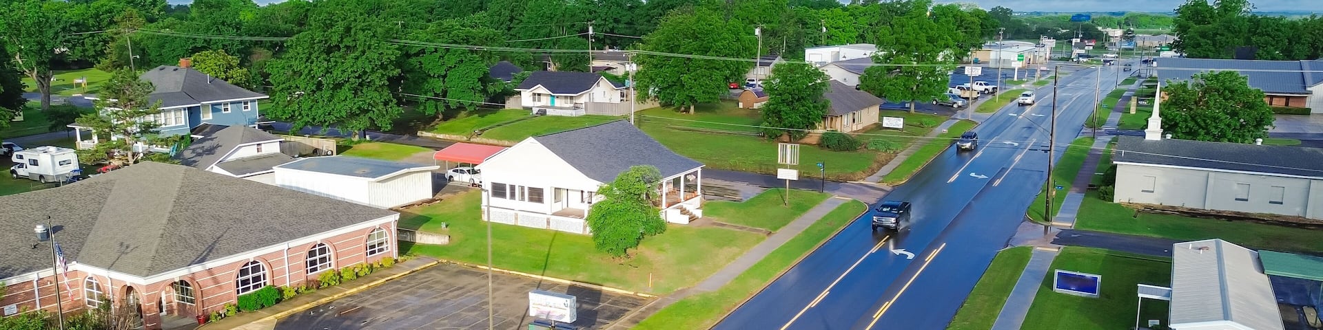 West Gentry Avenue in downtown Checotah, small town in McIntosh County, Oklahoma, mix of commercial buildings, churches, schools, residential neighborhood large houses, lush green trees, aerial