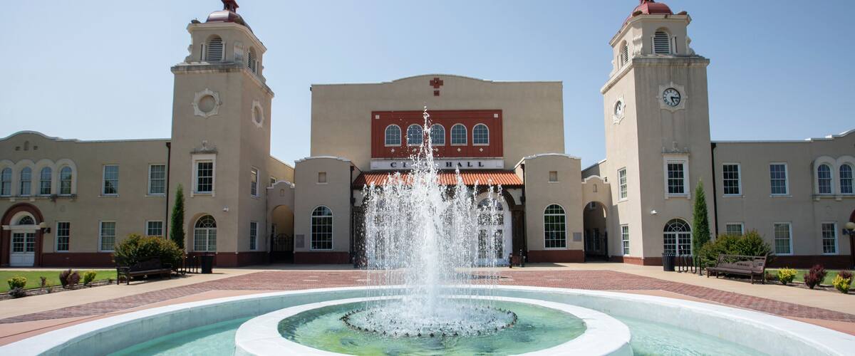 A fountain in front of a building with two towers and a clock.