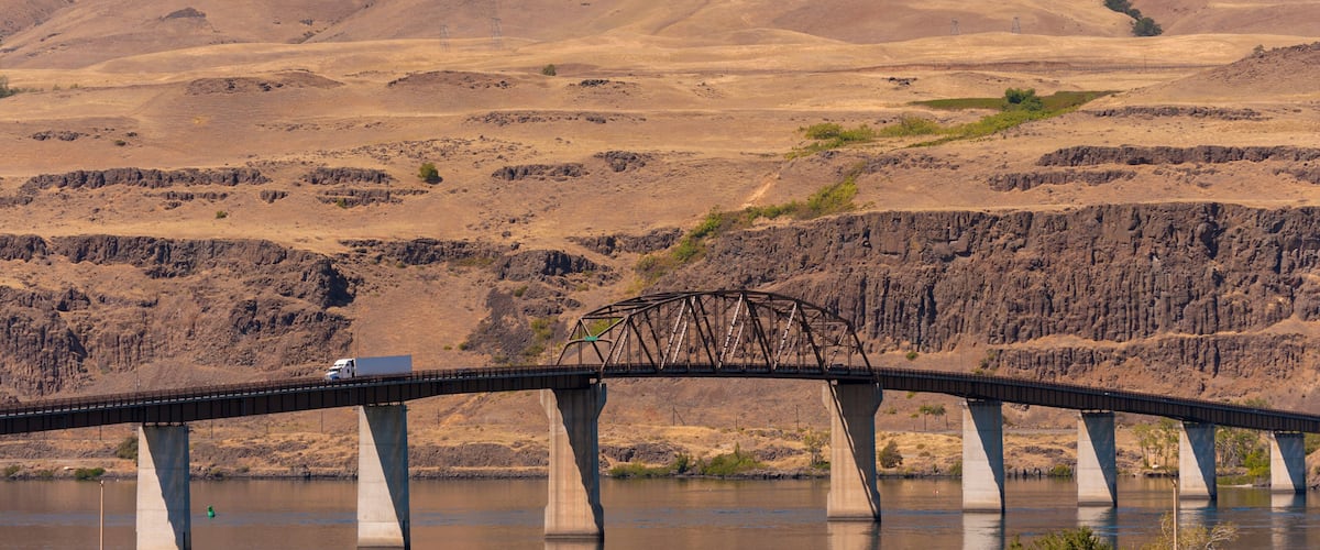 A bridge over a river with wind turbines in the background.