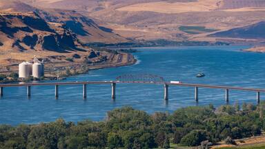 A river with a bridge, a dam, and hills in the background.
