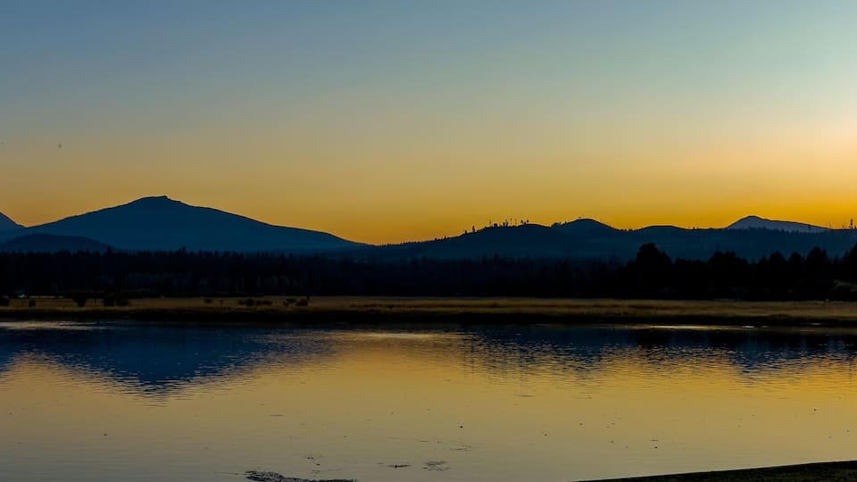 A mountain range at sunset with a calm lake reflecting the sky.
