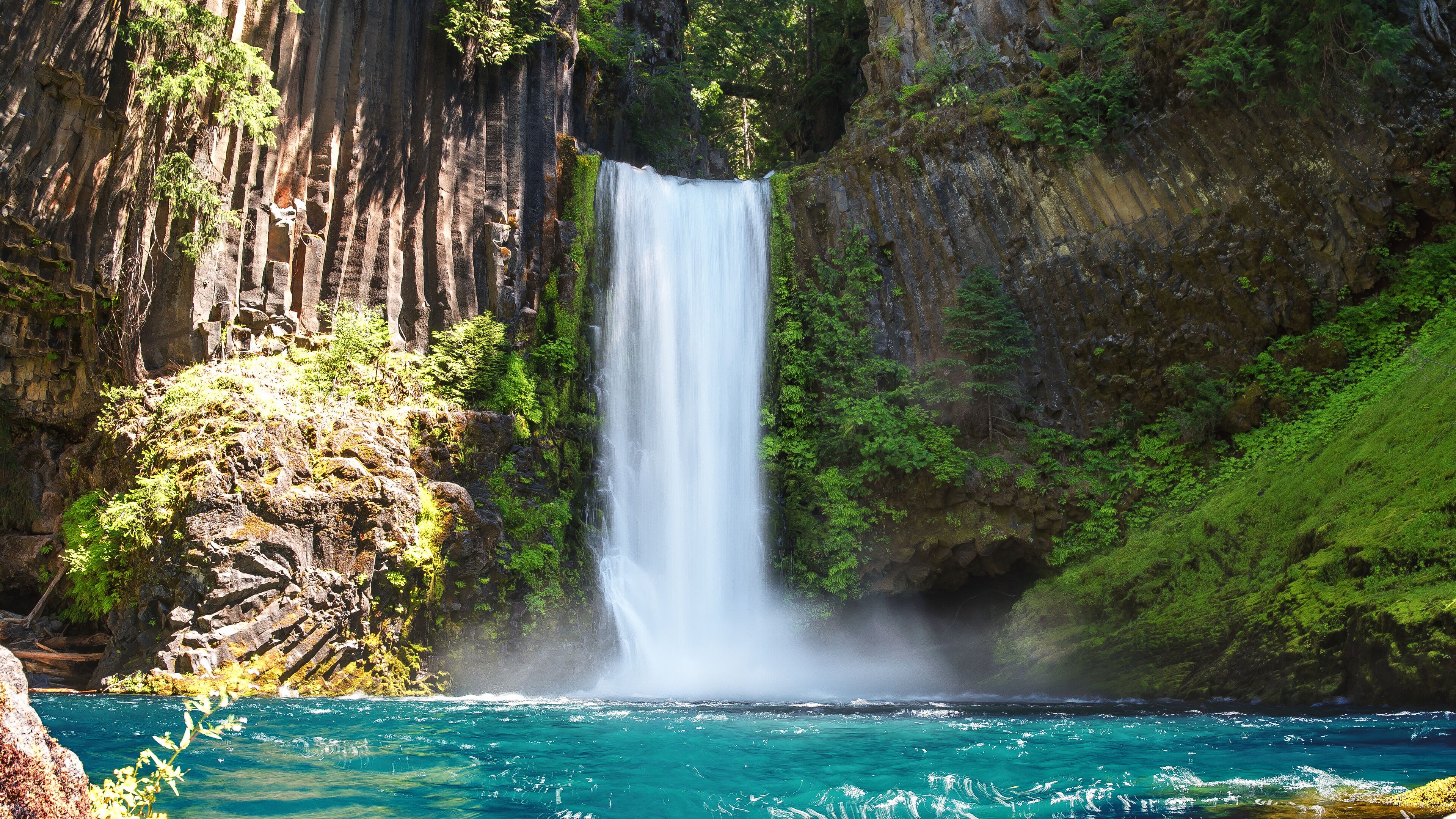 A waterfall cascading into a turquoise river surrounded by lush greenery and rocky cliffs.