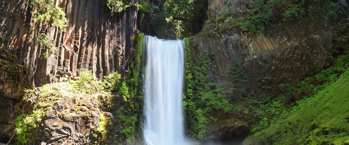 A waterfall cascading into a turquoise river surrounded by lush greenery and rocky cliffs.
