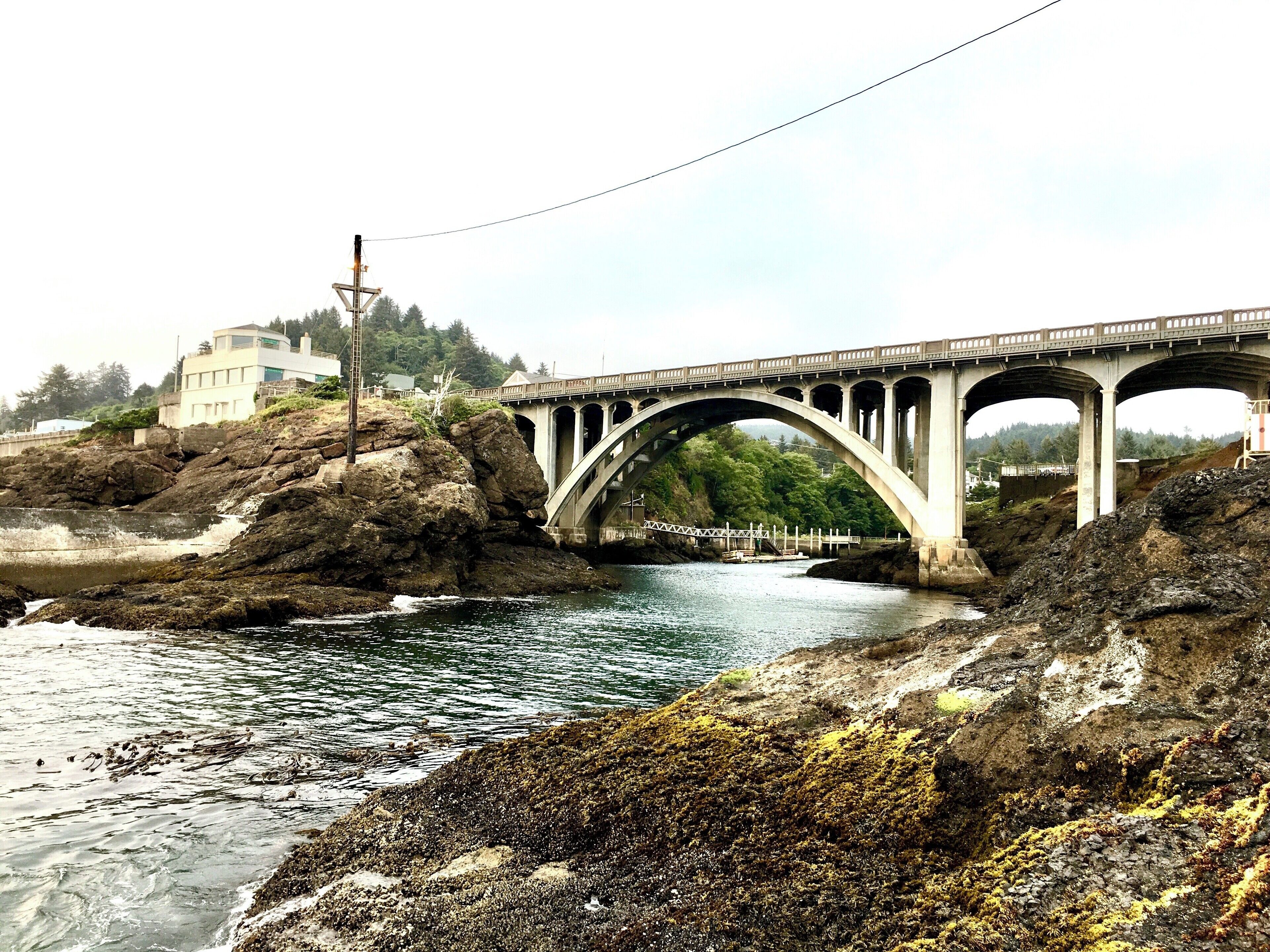 A stone bridge over a river with rocky shores and a building in the background.