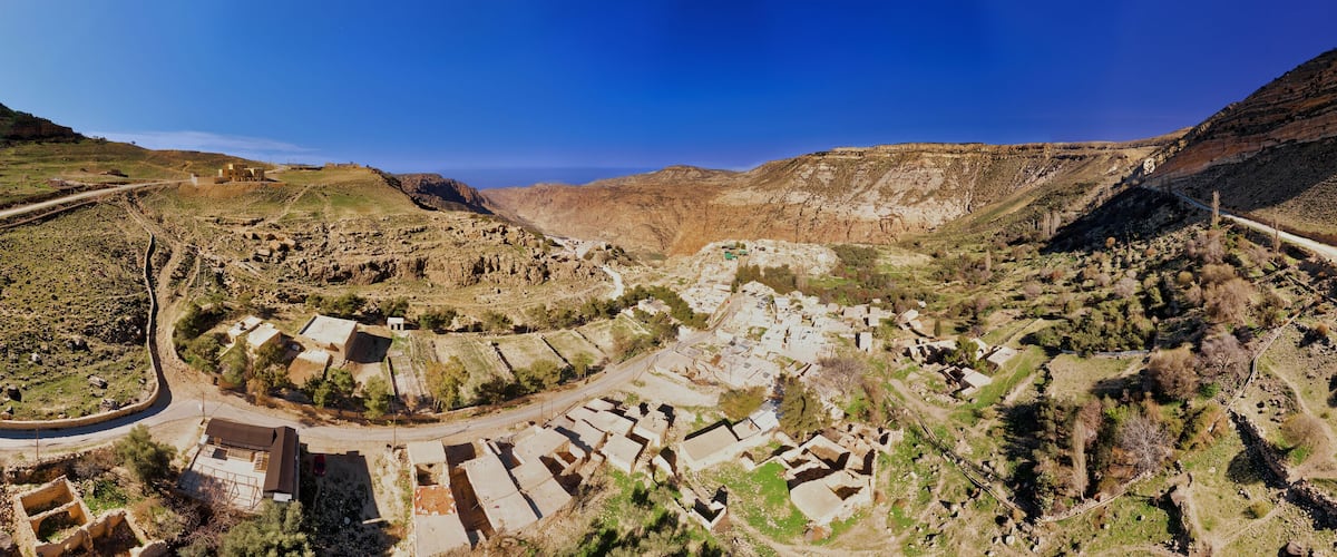 A panoramic view of a valley with a winding road, terraced fields, and a small settlement with buildings.