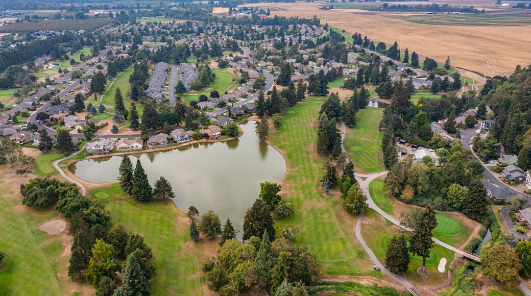 Aerial drone view of Staats Lake in Keizer, Oregon, near Salem, featuring a residential neighborhood, a golf course, and lush green landscapes under a clear blue sky
