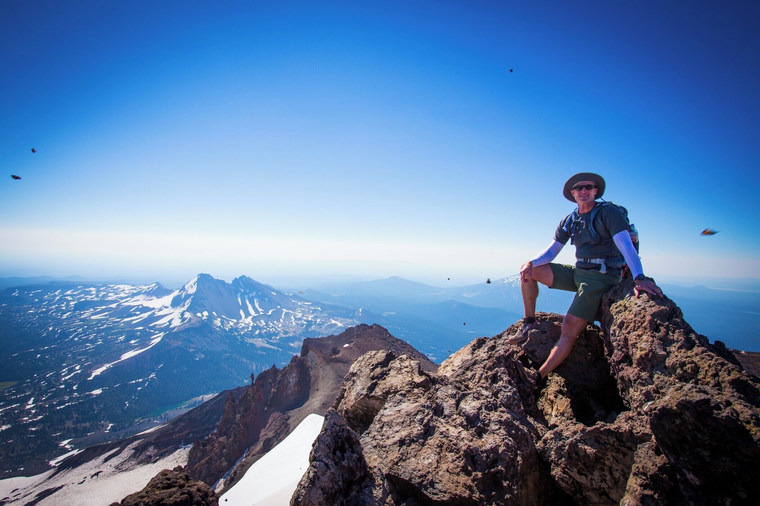 A person sitting on a rocky outcrop with a mountainous landscape in the background.