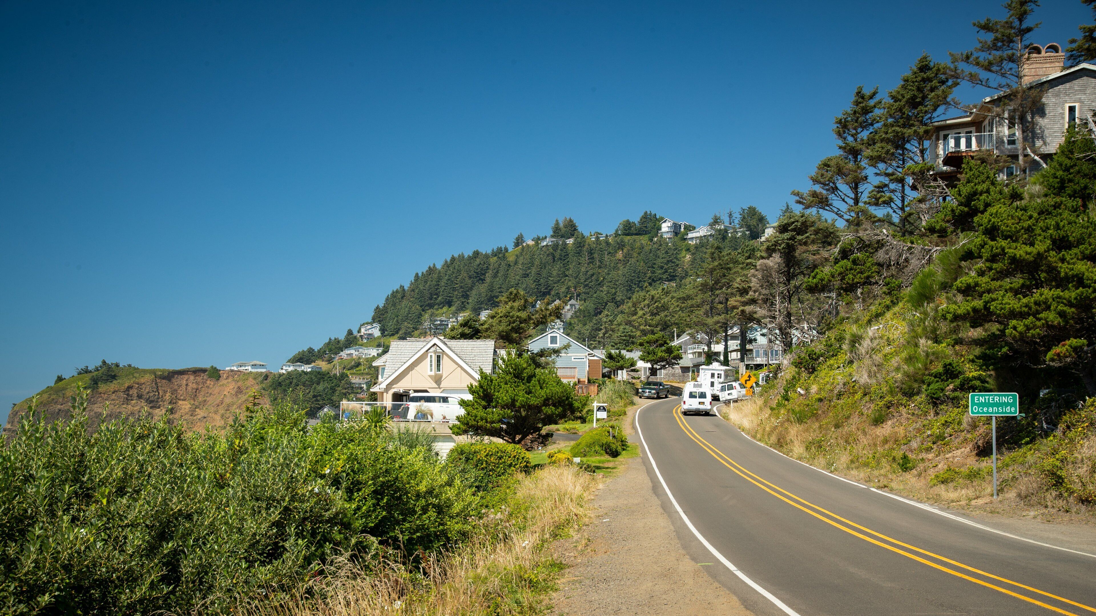 A coastal road with houses on a hillside, a clear blue sky, and a sign indicating 'ENTERING Oceanside'.