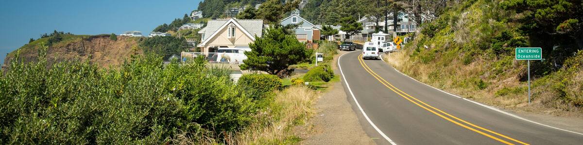 Une route côtière bordée de maisons construites sur une colline, un ciel bleu dégagé et un panneau indiquant « ENTRÉE à Oceanside ».