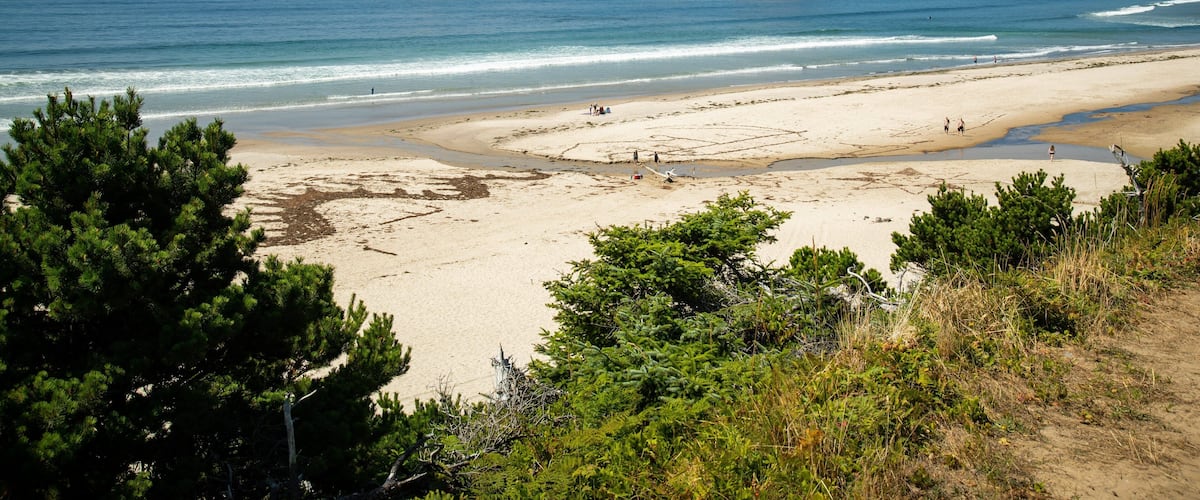 A beach with three large rock formations in the distance, surrounded by greenery and a clear blue sky.