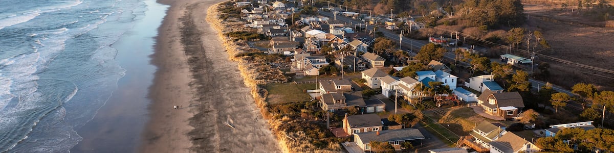 Une ville côtière avec une plage, des maisons et une colline boisée en arrière-plan.