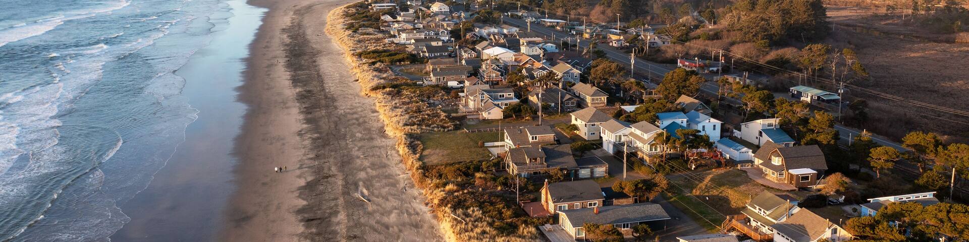 A coastal town with a beach, houses, and a forested hill in the background.