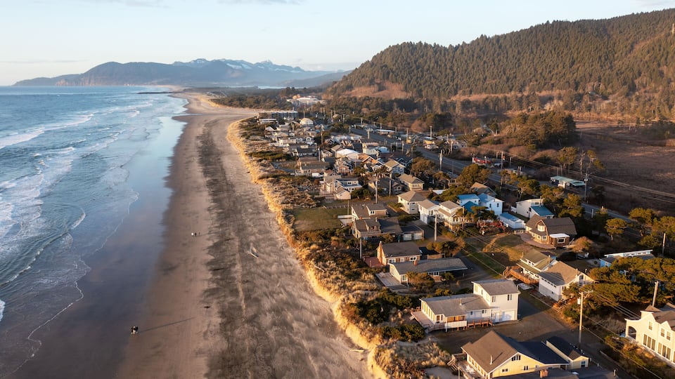 A coastal town with a beach, houses, and a forested hill in the background.
