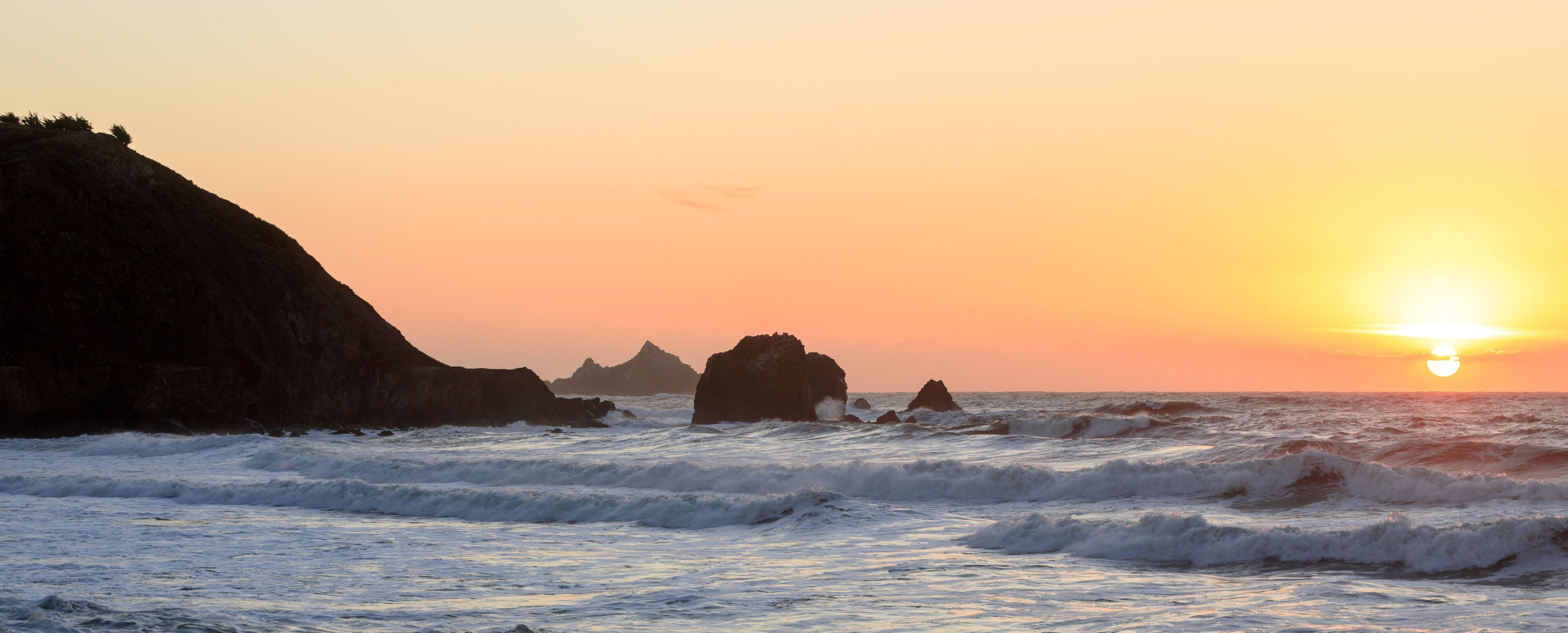 Atardecer sobre una costa rocosa con olas rompiendo contra las rocas.