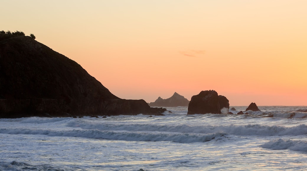 Atardecer sobre una costa rocosa con olas rompiendo contra las rocas.