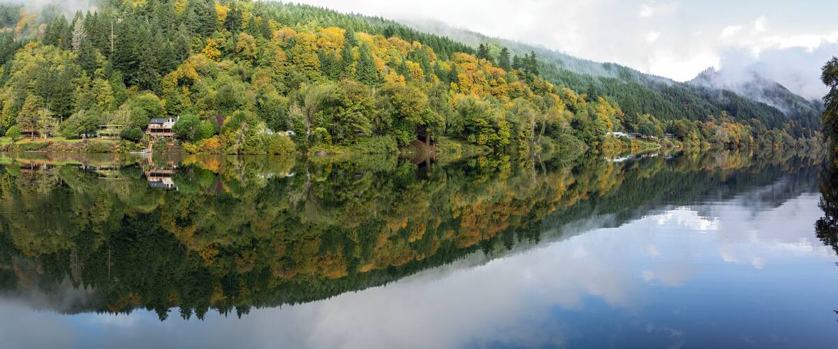 A serene lake with a reflection of a forested mountain and a small house on the shore.