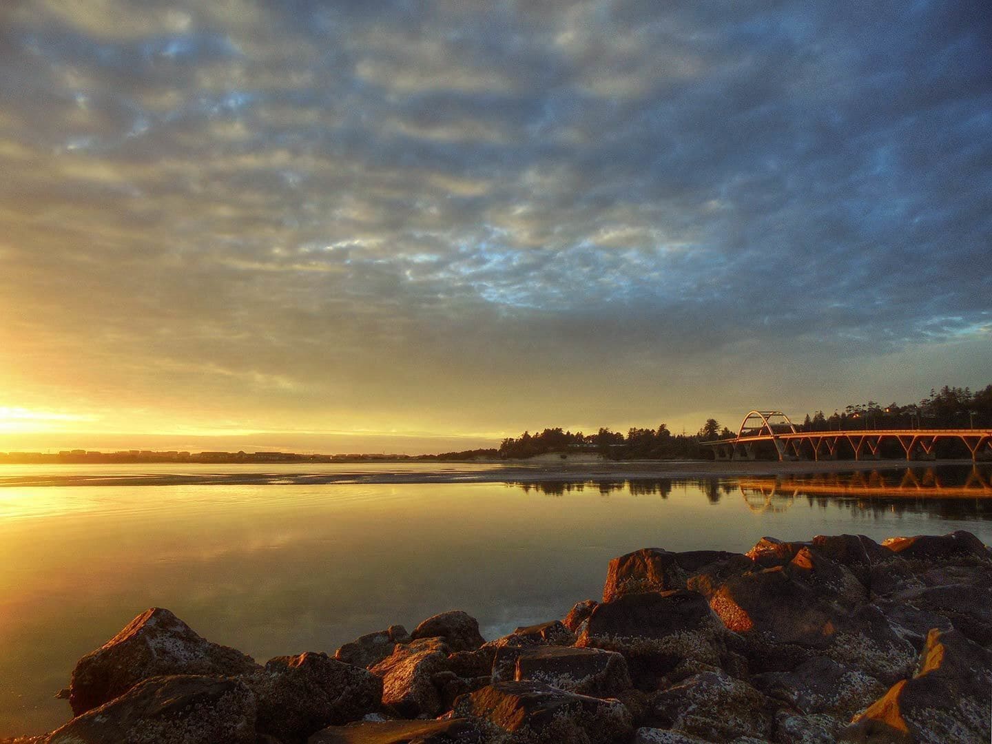A sunset over a calm lake with a bridge in the distance.