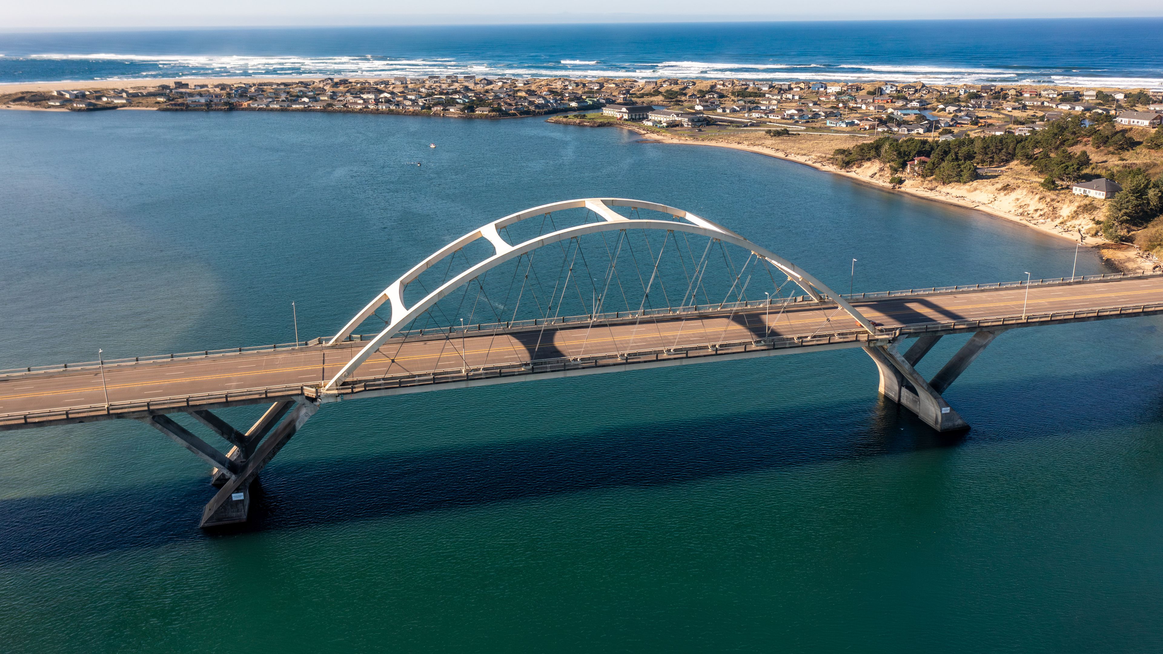 Vista aérea de un puente sobre un cuerpo de agua, con un pueblo costero al fondo.
