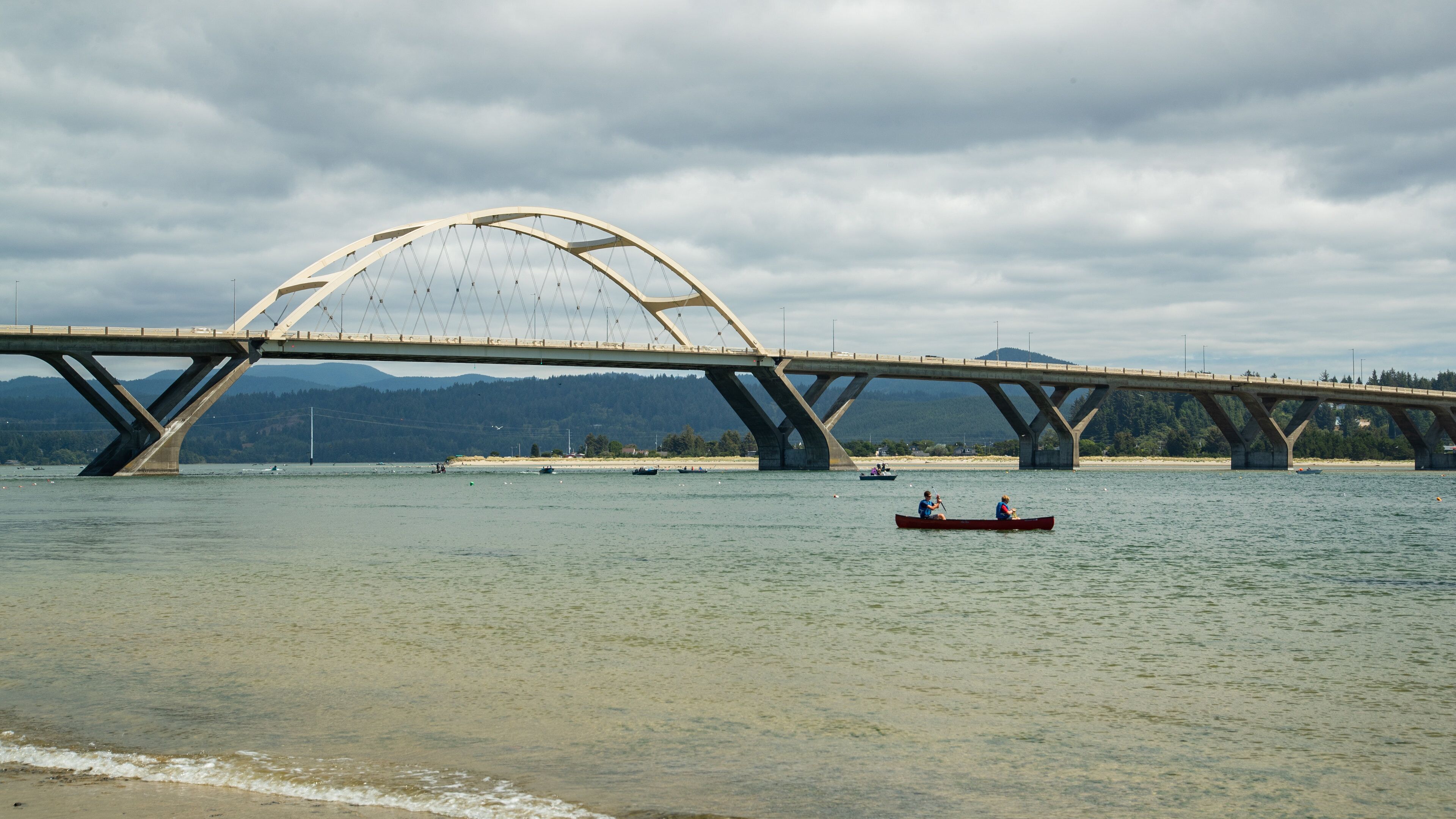 A large bridge spanning a river with a mountainous backdrop.