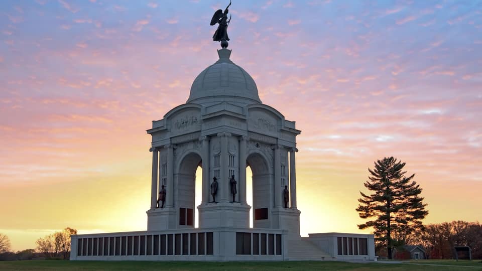 A white neoclassical building with a dome and statues, set against a sunset sky.
