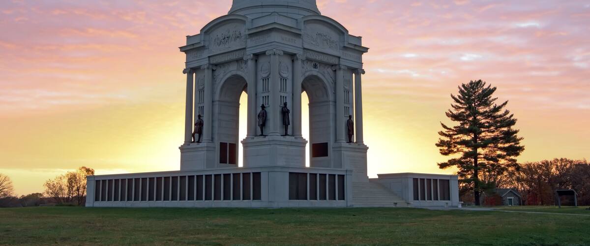 A white neoclassical building with a dome and statues, set against a sunset sky.