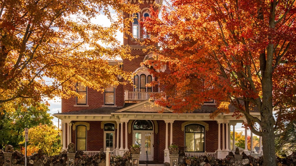 A Victorian-style house with a prominent tower, surrounded by autumn foliage.